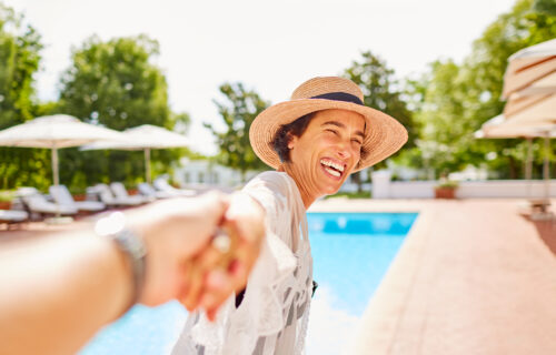 A very happy Arista San Gabriel resident being pulled to the pool, she is wearing a sun hat and a bathing suit cover up infront of a beautiful pool!